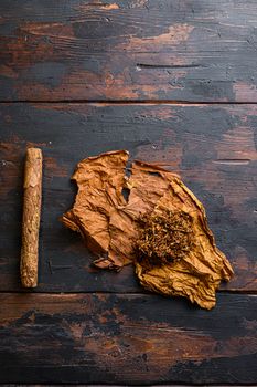 Cut tobacco and tobacco leaves with cigar on background on vintage dark table. overhead shot top view space for text.