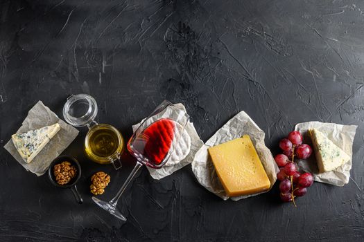 Assortment of cheeses, Camembert antipasto a glass of red wine, honey, nuts and spices, on a black backdrop stone slate Top view. Free space for text top view.