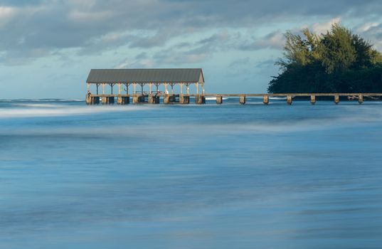 Sunrise lights the dawn sky above Hanalei Pier with long duration exposure to blur waves near Hanalei, Kauai, Hawaii