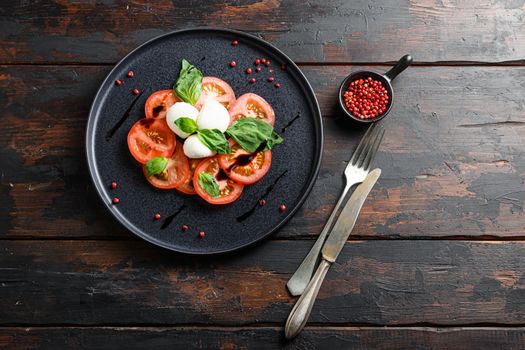 caprese salad with sliced tomatoes, mozzarella cheese, basil, olive oil. Served on black plate wood kitchen old rustic table top view flatlay space for text.