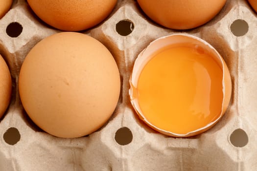 Top view has broken egg with the yolk in the paper carton.