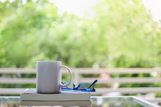 Hobby, Relaxation and Recreation Concept. Close up of white mug cup of hot coffee with reading glasses and books in garden with copy space.