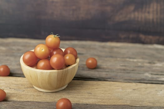 Group tomato in a wood bowl place on the wooden table. Cherry tomatoes is a small that has a sweet, firm texture and has a pleasant aroma. And contains beta-carotene, vitamin C and high vitamin E.