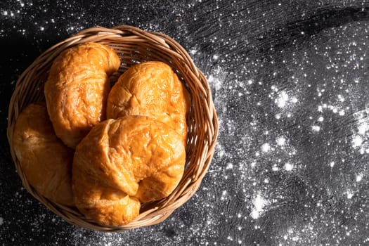 Top view Croissants in a wicker basket placed on a black floor which makes pastry dough