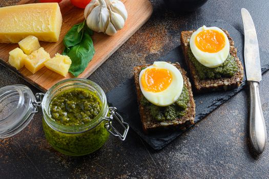 homemade eggs panini bread with Green basil pesto in glass jar silver spoon on italian breakfast with ingredients green pesto on gmetal surface table close up