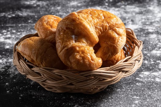Close-up Croissants in a wicker basket placed on a black floor which makes pastry dough