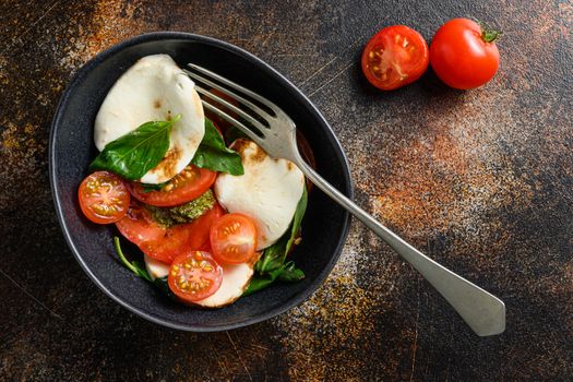 Tomato, basil, mozzarella Caprese salad ib bowl with fork with balsamic vinegar and olive oil. old rustic background over head top view.