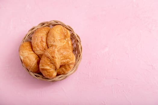 Top view croissants in the wooden basket on the pink background and texture.