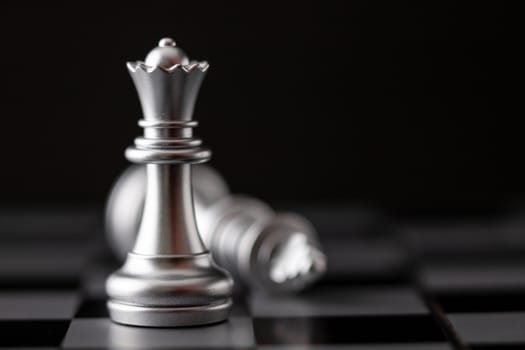 Silver queen standing and king falling in game on the chessboard