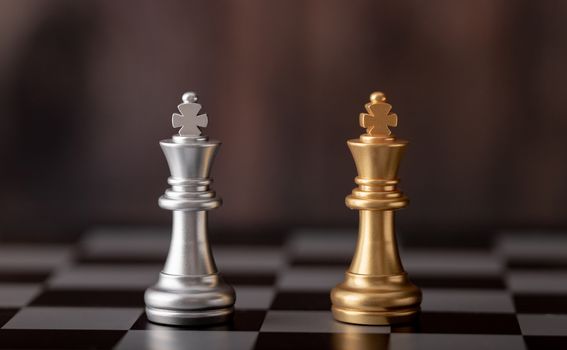 gold and silver king standing on chess board with wooden background