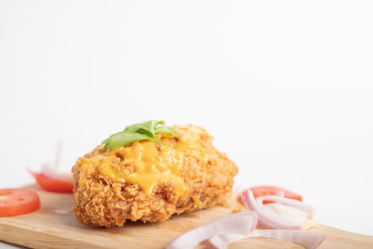 Chicken fried topped cheese on the wooden cutting board with onions and tomato sliced and the white background