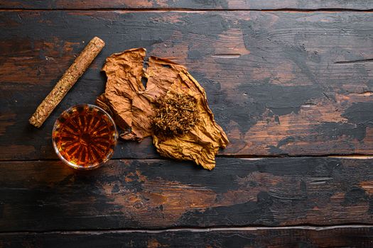 Dried tobacco leave and cut tobacco with cigar and whiskey rum on wood background on vintage dark table. top view space for text.