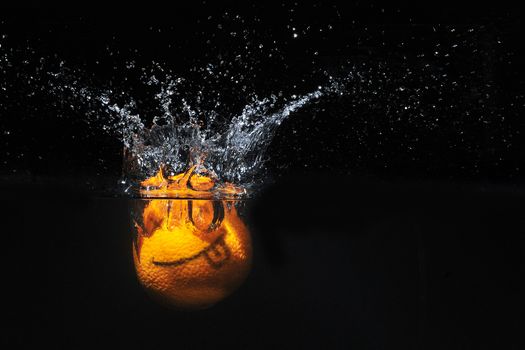 Smile orange with splashes of water on a black background