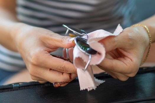 Woman hands cleaning her sun glasses with micro fiber cloth wipe, wiping sunglasses