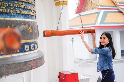 Woman ringing a bell in a Buddhist temple in Thailand