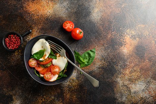 Tomato, basil, mozzarella Caprese salad ib bowl with fork with balsamic vinegar and olive oil. old rustic background over head top view space for text horizontal photo.