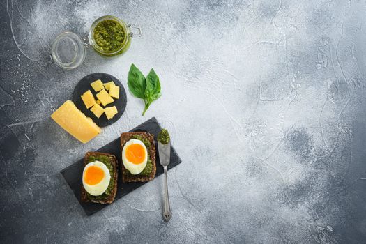 homemade eggs panini bread with Green basil pesto silver spoon on italian breakfast with ingredients green pesto on grey and white concrete table surface overhead top view space for text lay flat.