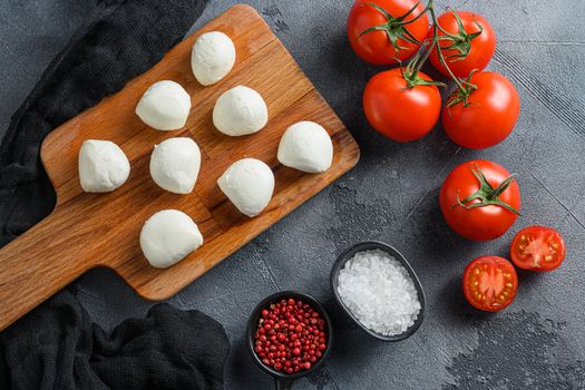Buffalo Mozzarella cheese balls with fresh basil leaves and cherry tomatoes, the ingredients of the Italian Caprese salad, on a black cloth and grey concrete background.