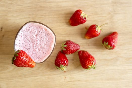 Fresh strawberry smoothie cold drink. Milkshake in glass on wooden table. Fruits for decoration