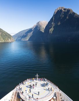 Passengers on cruise ship sailing into Milford Sound on South Island of New Zealand in early morning as the sun rises above the mountains