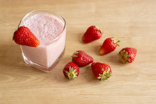 Fresh strawberry smoothie cold drink. Milkshake in glass on wooden table. Fruits for decoration