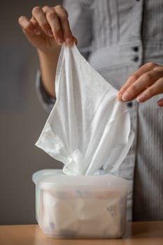 Wet wipes are universal an practical: woman hand take one wipe from big plastic box package for cleaning, home, indoor