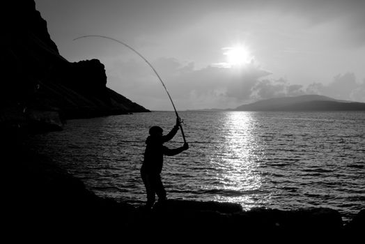 sunsets over loch na keal on the isle of mull as a young man fishes for mackerel in black and white