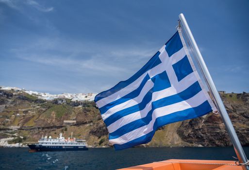 Greek flag on tender boat leaving Fira port on Santorini