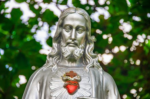 Jesus Christ grey statue with red heart over foliage