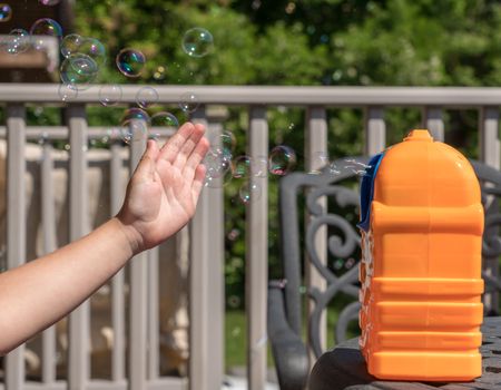 Childrens toy soap bubble blower with young girl hand hitting the bubbles being blown