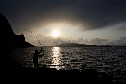 sunsets over loch na keal on the isle of mull as a young man fishes for mackerel in Color