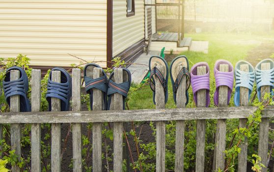 Summer shoes flip flops for a happy friendly family hang on a wooden fence outdoors on a Sunny summer day.