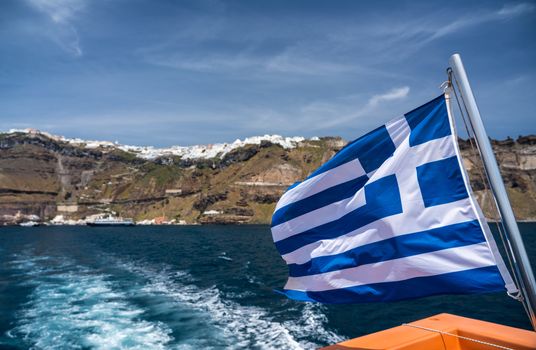 Greek flag on tender boat leaving Fira port on Santorini