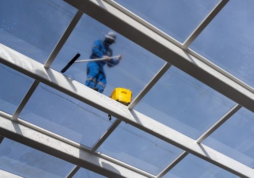 Male worker washing large expanse of glass roof over swimming pool