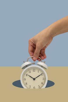 Hand holding white vintage alarm clock  on blue backdrop falling down. Time Minimal concept.