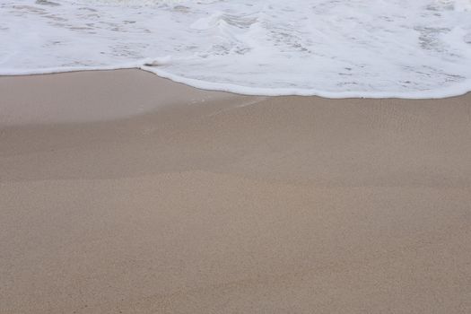 Wave of the sea and white clean foam on the sandy beach with Copy space.