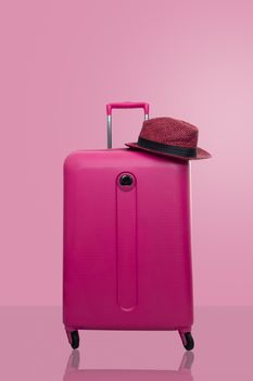 Pink suitcase with hat  on pastel pink background. travel concept. minimal style.