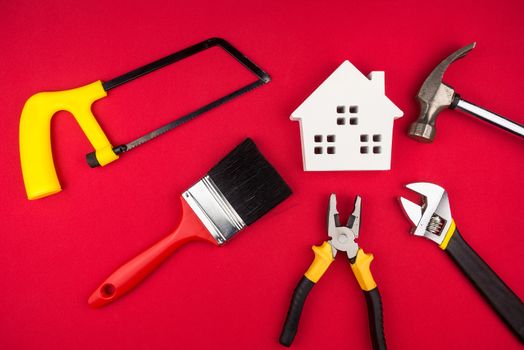Wooden white house and construction tools on red background with copy space.Real estate concept, New house concept, Finance loan business concept, Repair maintenance concept.