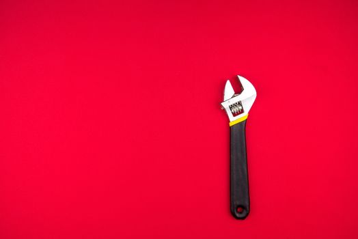 Adjustable wrench with black rubberized handle, on red background.Top view. Space for text