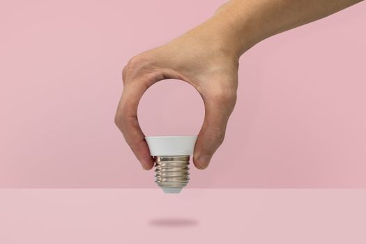 Hand holding a light bulb shape isolated on pink background, minimal idea concept.