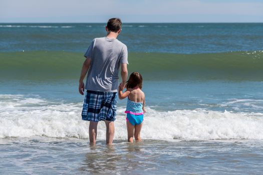 Back view of father and young girl facing the sea waves as concept for protection against future problems