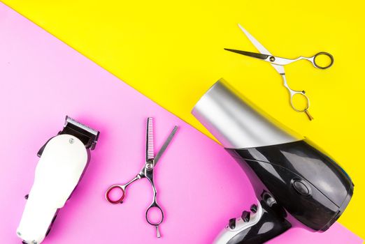 Stylish Professional Barber Scissors, White electric clippers and hair dryer on yellow and pink background. Hairdresser salon concept, Hairdressing Set. Haircut accessories. Copy space image, flat lay