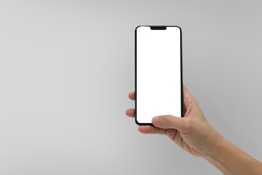 Hand holding black mobile phone with blank screen isolated on gray background.