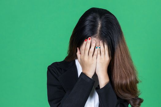 Frustrated stressed young Asian business woman with hands on face in depression on green isolated background.