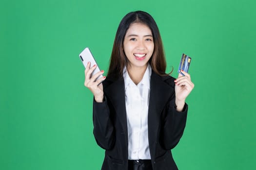 Portrait of cheerful young Asian business woman holding mobile smart phone and credit card on green isolated background.