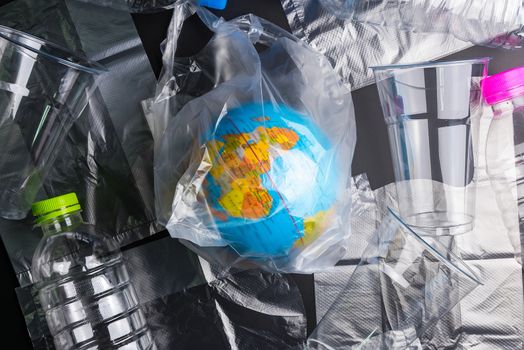 Earth world globe and plastic bottle waste on the black background.Saving the planet Earth from plastic bags concept.Global warming.Plastic waste overflows the world