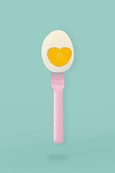 Half boiled egg on a pink fork on blue background, minimal eater concept.