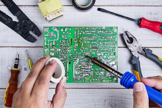 Serviceman soldering circuit board with soldering iron in the service workshop.