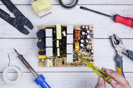Serviceman check circuit board with electrical tester screwdriver in the service workshop.