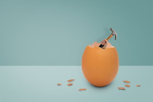 Holding the hammer out of the egg shell on blue background, easter concept.